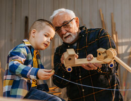 A man shows a handmade wooden toy to his grandson.